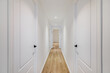 Interior of long narrow hallway with closed doors, wooden floor and white walls in apartment designed in minimal style.