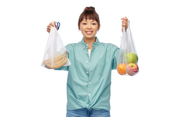 Sticker - sustainability, eco living and people concept - portrait of happy smiling young asian woman holding reusable bag with bananas and plastic bag with apples over white background