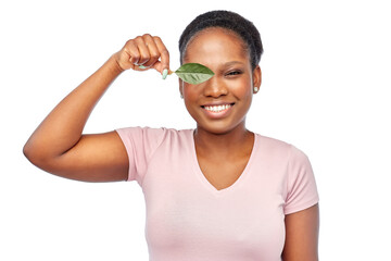 Poster - eco living, environment and sustainability concept - portrait of happy smiling young african american woman covering one eye with green leaf over white background