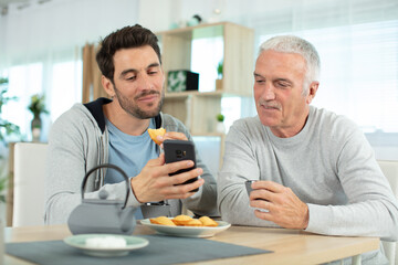 Wall Mural - an adult hipster son and senior father in the kitche