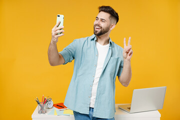 Wall Mural - Young employee business man in shirt stand work at white office desk pc laptop do selfie shot on mobile phone post photo on social network show victory gesture isolated on yellow background studio