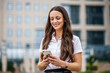 © djoronimo - Portrait of happy businesswoman typing on smartphone in front of company building.
