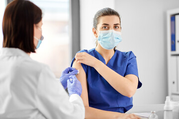 Wall Mural - healthcare, medicine and pandemic concept - female doctor or nurse wearing protective mask with syringe vaccinating medical worker hospital