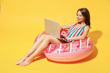 Wall Mural - Full body length happy young sexy woman wear red blue swimsuit sit on inflatable ring work on pc laptop isolated on vivid yellow color background studio Summer hotel pool sea rest sun tan concept