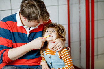 Wall Mural - Father helping his little daughter with brushing teeth. Little toddler girl and dad in bathroom, making hygiene actions. Happy family, man and child. Morning routine with children.