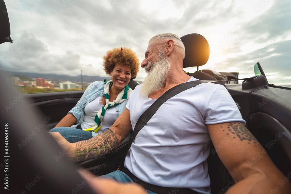 Happy senior couple having fun driving on new convertible car - Mature people enjoying time together during road trip tour vacation - Travel people lifestyle concept - obrazy, fototapety, plakaty 