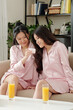 © DragonImages - Beautiful young female friends in silk pajamas drinking orange juice and testing new body lotion or face cream