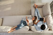 © New Africa - Happy couple with tablet and book on sofa in living room, above view