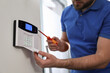 © New Africa - Man installing home security system on white wall in room, closeup