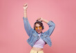 © NaMong Productions - Happy beautiful Asian teen woman in yellow glasses listening music in headphones and dance on pink background.