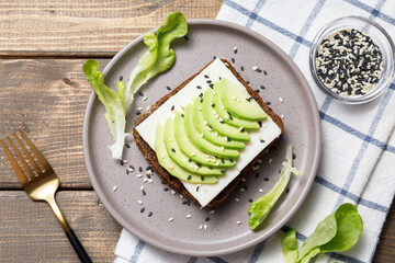 Rye bread toast with goat cheese and avocado on wooden table background. Healthy avocado open sandwich for breakfast or lunch. Flat lay, top view