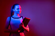 Digital lifestyle. Futuristic technology. Virtual business. Curious smart confident woman with laptop in pink blue fluorescent neon light isolated on purple empty space background.