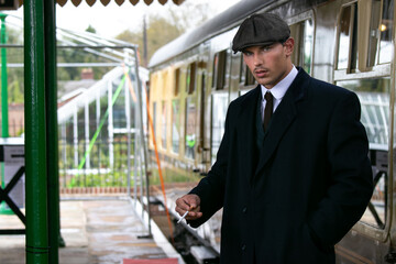 Wall Mural - Handsome English gangster smoking at railway station with train in the background