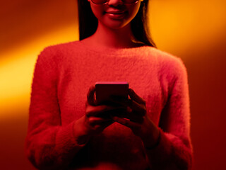 Gadget people. Mobile communication. Social media. Virtual lifestyle. Pink neon light smiling girl using phone isolated on yellow golden color gradient background.