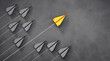 Group of paper airplanes with yellow leader plane on dark background