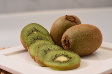 white square plate with sliced kiwi and two whole kiwis