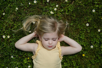 outdoor portrait of toddler girl with long blonde hair laying down on a green meadow