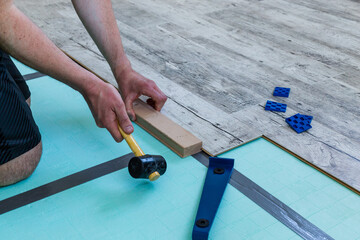 Man laying laminate flooring using a set of tools.