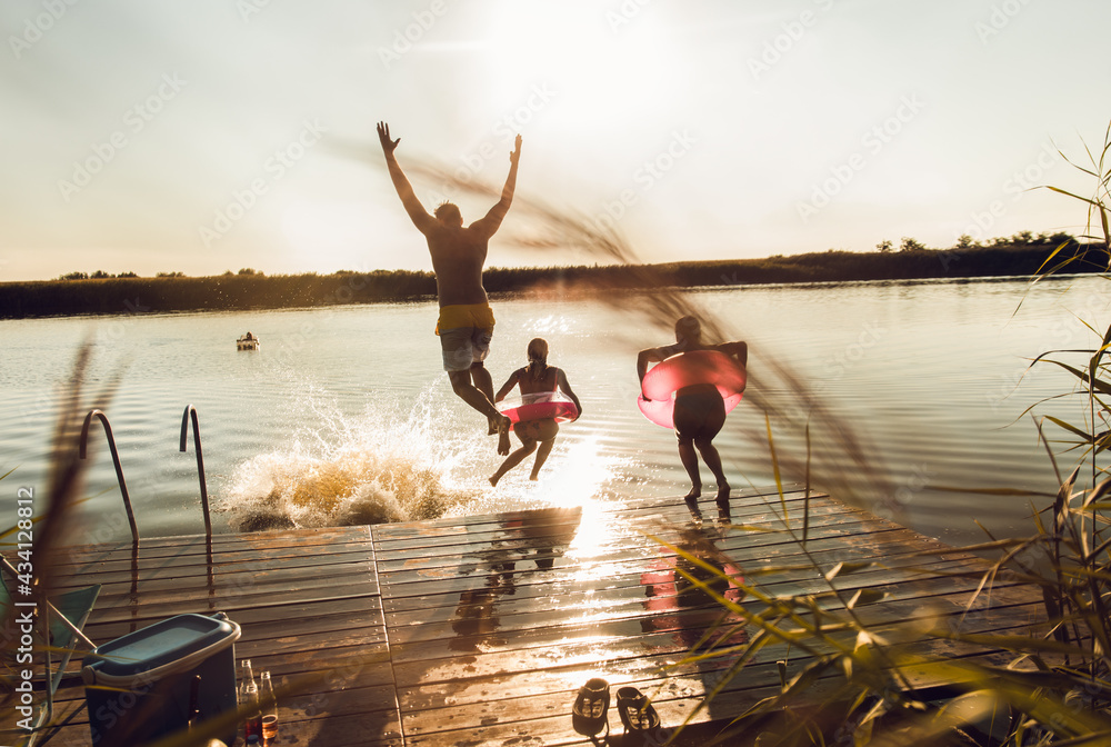 Friends having fun enjoying a summer day swimming and jumping at the lake. - obrazy, fototapety, plakaty 