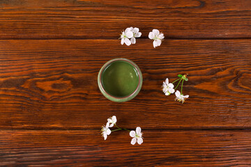 Wall Mural - Green tea in a ceramic cup with cherry flowers on a wooden background. Top view.