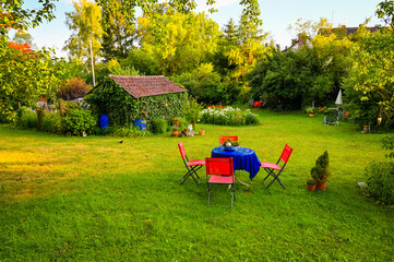 Beautiful garden with a garden table and chairs in the front and a garden hut in the background. The golden evening sun illuminates this peaceful place.