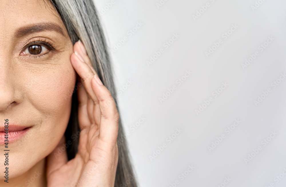 Closeup cut portrait of happy middle aged mature asian woman, senior older 50 year lady looking at camera touching her face isolated on white. Ads of eye lifting anti wrinkle skin care cream. - obrazy, fototapety, plakaty 