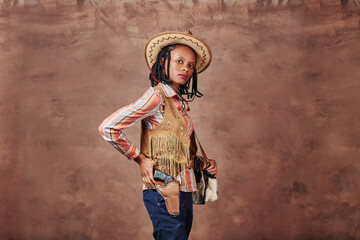 portrait of an african american girl cowboy with hat and pistol in holster. photo in the studio. brown background