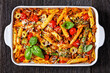 ground turkey penne pasta bake with asparagus, tomatoes and olives in a baking dish on a dark wooden table, italian cuisine, flat lay, close-up