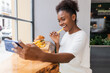 © Julio Rodriguez/ADDICTIVE STOCK - Side view joyful young African American female in white blouse enjoying delicious French fries and burger while taking selfie on smartphone in fast food restaurant