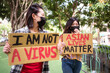 © Juan Alberto Ruiz/ADDICTIVE STOCK - Ethnic females in masks holding posters protesting against racism in city street and looking away