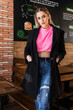 © Julio Rodriguez/ADDICTIVE STOCK - Attractive young female in jeans pink sweater and black coat standing with hands in pockets near table in restaurant and looking at camera