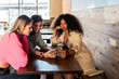 © Julio Rodriguez/ADDICTIVE STOCK - Young stylish female friends browsing mobile phones while sitting at table in cafeteria