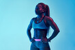© Manuel Ruiz/ADDICTIVE STOCK - Young muscular African American female athlete in sports clothes with Afro braids and hands on hips looking away in neon light