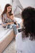 © LIGHTFIELD STUDIOS - happy mother sitting with son and looking at african american doctor on blurred foreground