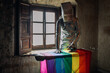 © Sergio Victor Vega/ADDICTIVE STOCK - Unrecognizable person in silver costume and box on head ironing LGBTQ flag while standing in shabby abandoned room