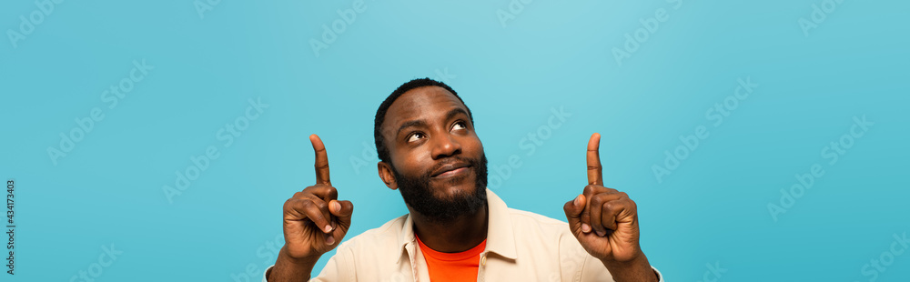smiling african american man pointing up with fingers isolated on blue, banner - obrazy, fototapety, plakaty 