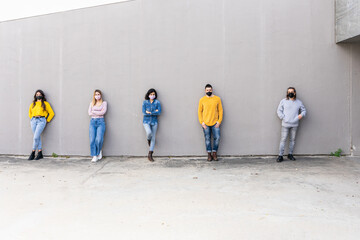  Group of young millennials on the grey wall with face mask smiling and looking the camera - Friends after the lockdown for protection by Corona Virus, Covid-19 at the social distance - Copy space