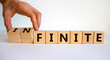 Finite or infinite symbol. Businessman turns wooden cubes and changes the word 'finite' to 'infinite'. Beautiful white table, white background. Business, finite or infinite concept. Copy space.