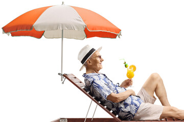 Wall Mural - Elderly man relaxing on a beach bed under umbrella with a cocktail