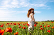 Beautiful girl posing in a poppy field. A woman with a hat stands in the middle of flowers. The young girl smiles. Happiness concept. Relaxing on summer poppy flowers meadow.