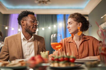 Wall Mural - Portrait of elegant mixed-race couple enjoying dinner with friends indoors and looking at each other