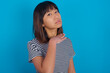 young beautiful asian woman wearing stripped t-shirt against blue wall cutting throat with hand as knife, threaten aggression with furious violence.