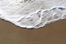 White, Foamy Remnant Of A Wave Washing Up On Smooth Wet Sand