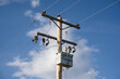 A wooden power pole and transformer with communication and transmission lines under a blue sky background.
