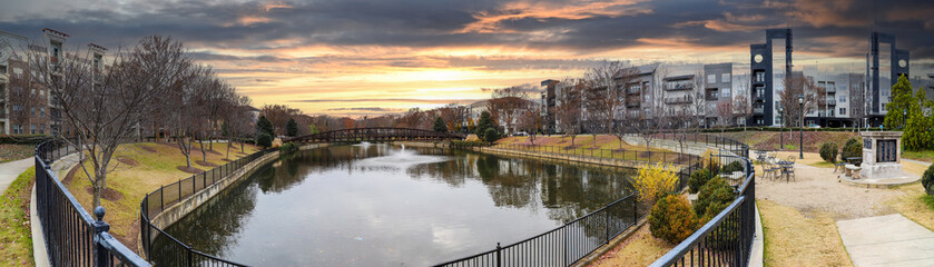 a stunning panoramic shot of a still lake with an iron bridge and a fountain in the middle of the lake with green and autumn colored trees and plant at The Commons park in Atlanta Georgia USA