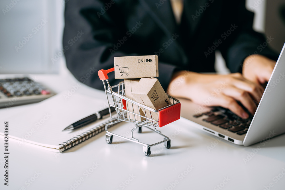 card box small in shopping cart with businesswomen using laptop on a desk, e-commerce, and delivery online business concept. - obrazy, fototapety, plakaty 