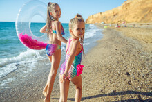 Children Are Playing On The Beach. Children Swim And Play In The Sea On Summer Family Vacations. Sand And Water Activities. Two Girls Run On The Ocean Shore. High Quality Photo.