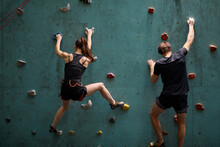 Fitness, Extreme Sport And Healthy Lifestyle Concept. Young Couple Bouldering On Rock Climbing Wall At Indoor Gym, Rear View On Young Man And Woman Engaged In Sport, Preparing For Competition