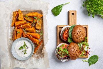 Meat free plant based burger served with sweet potato wedges, green mix salad and white sauce on gray table. Healthy vegan or vegetarian food concept. Top view.