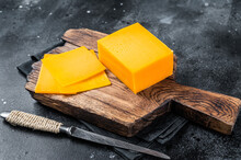 Slices Of Cheddar Cheese On A Wooden Cutting Board. Black Background. Top View